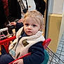 toddler, child, shopping_cart, pacifier, fleece_vest, blue_eyes, adult, black_cardigan, shopping, indoor, clothing, hand, face, person, retail, store, casual, curly_hair, red_cart, portrait