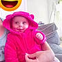 baby, child, pink_hoodie, smiling, happy, indoor, couch, adult_hand, cute, hooded_jacket, infant, person, home, cozy, plush_clothing, face, portrait, casual, seated, joyful