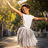 Asena is registered to the contest to win money with this photo: child, tutu, angel_halo, white_shirt, outdoor, sunlight, street, pose, dress_up, costume, bokeh, curly_hair, happy, fashion, playful, smile, nature, tree, performance, portrait