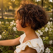 Asena is registered to the contest to win money with this photo: child, side_profile, curly_hair, golden_hour, sunlight, flower, white_flower, outdoor, nature, park, greenery, portrait, summer, daylight, young, person, dress, white_dress, beautiful, peaceful