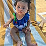 toddler, child, beach_towel, swimsuit, curly_hair, blue_swimsuit, striped_towel, outdoor, sunny, barefoot, sitting, cute, expression, young_child, summer, playful, vacation, sand, daylight, person