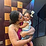 woman, baby, child, kiss, love, smile, curly_hair, bow, purple_dress, jeans, indoor, staircase, wooden_panel, affection, family, holding, person, portrait, happy, home