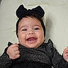 baby, smiling, black_bow, black_clothing, cushion, happy, infant, child, headband, portrait, cute, indoors, person, fashion, sitting, young_child, face, hands, joy, expression