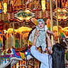Gemma is registered to the contest to win money with this photo: baby, adult, carousel, horse, amusement_ride, lights, colorful, joy, smile, headband, overalls, hand, fun, carnival, entertainment, person, child, bright, festival, play