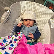 Micheal joined the competition — help win amazing prizes! baby, infant, hat, bib, blanket, baby_seat, floor, toy, indoor, child, face, clothing, cushion, pink_blanket, patterned_blanket, wooden_floor, pacifier, person, cute, young_child