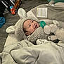 baby, smiling, hoodie, plush_toy, elephant, blanket, pacifier, indoor, floor, toy_truck, wooden_floor, child, cute, warm_clothing, infant, happy, face, headwear, soft_texture, cozy