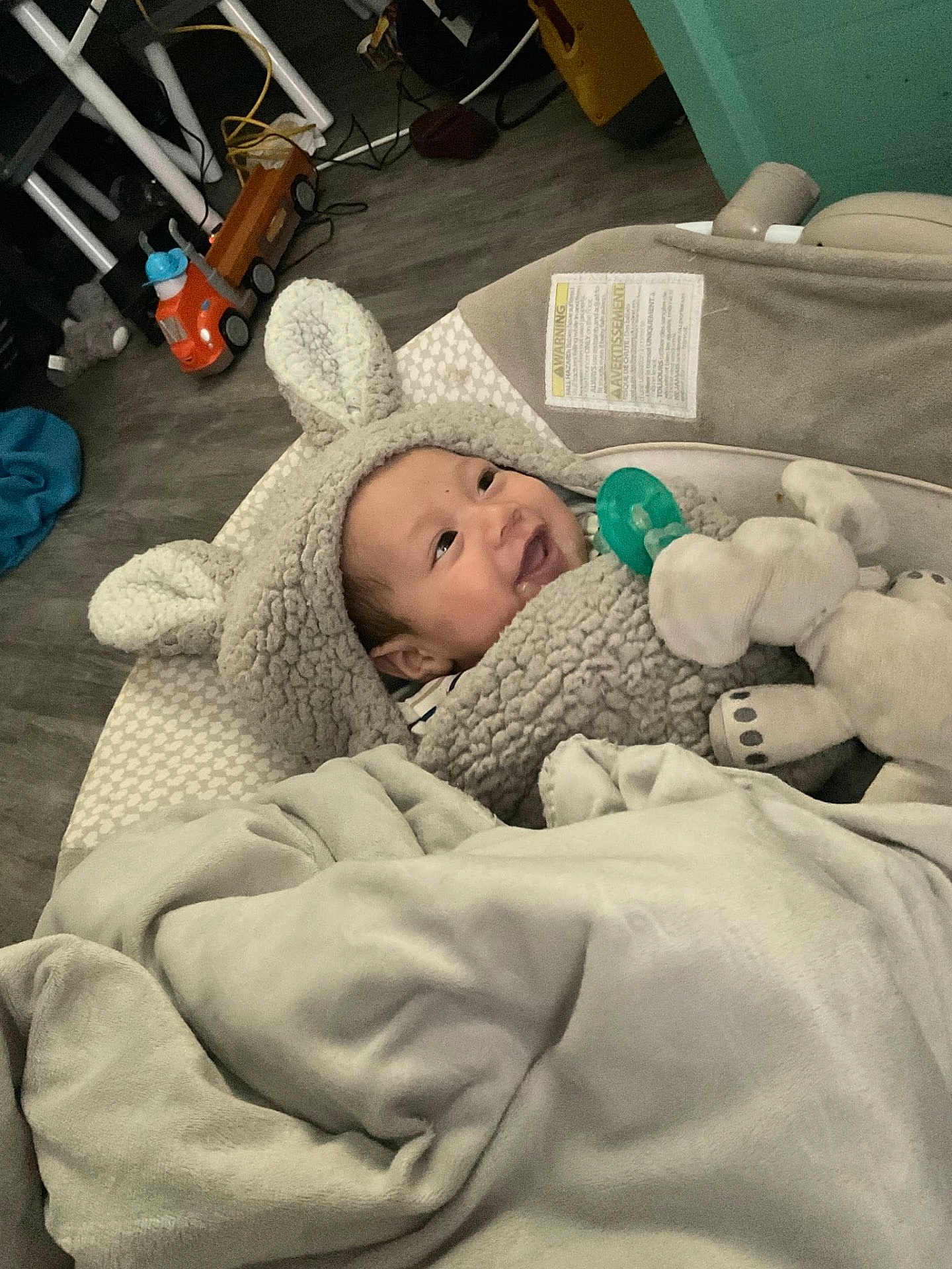 Micheal joined the competition — help win amazing prizes! baby, smiling, hoodie, plush_toy, elephant, blanket, pacifier, indoor, floor, toy_truck, wooden_floor, child, cute, warm_clothing, infant, happy, face, headwear, soft_texture, cozy