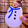 baby, background, black_icing, blue_icing, child, christmas, cookie, cute, face, festive, food, hand, holiday, icing, indoor, person, plaid_blanket, portrait, santa_hat, snowman