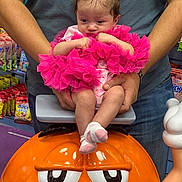 Kehlani is registered to the contest to win money with this photo: baby, child, tutu, pink_clothing, butterfly_hair_clips, orange_cartoon_character, adult_hands, casual_clothing, snack_packages, store_interior, jeans, tshirt, indoor, cute, pensive, small_feet, socks, colorful, toy, holding