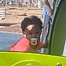 toddler, child, pacifier, playground, outdoor, park, play_equipment, colorful, green, blue, person, curly_hair, daylight, urban, trees, bench, grass, clothing, smile, baby