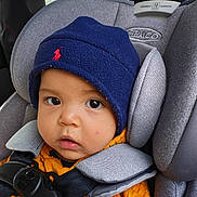Bryson is registered to the contest to win money with this photo: baby, child, car_seat, seatbelt, hat, clothing, orange_sweater, blue_hat, face, eyes, infant, car_interior, safety_harness, headrest, person, portrait, closeup, cute, warm_clothing, young_child
