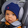 baby, child, car_seat, seatbelt, hat, clothing, orange_sweater, blue_hat, face, eyes, infant, car_interior, safety_harness, headrest, person, portrait, closeup, cute, warm_clothing, young_child