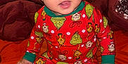 Bryson is registered to the contest to win money with this photo: baby, child, pajamas, grinch, bed, blanket, orange_bedspread, red_blanket, indoor, person, smiling, cute, sitting, foot, hand, head, face, clothing, infant, cozy