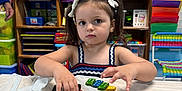 Taliah is registered to the contest to win money with this photo: child, girl, toy, dice, classroom, education, play, pigtails, bows, table, colorful, learning, preschool, furniture, storage, shelf, plastic, cute, indoor, person