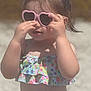 child, toddler, sunglasses, heart_shaped, swimsuit, floral_pattern, beach, sunny, outdoor, summer, hair_tie, pink, playing, sunlight, cute, fashion, portrait, person, skin, hands