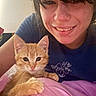 person, woman, cat, kitten, orange_cat, pet, cuddling, smiling, portrait, selfie, indoors, blue_shirt, pink_blanket, brown_hair, whiskers, ears, eyes, close_up, home, cute