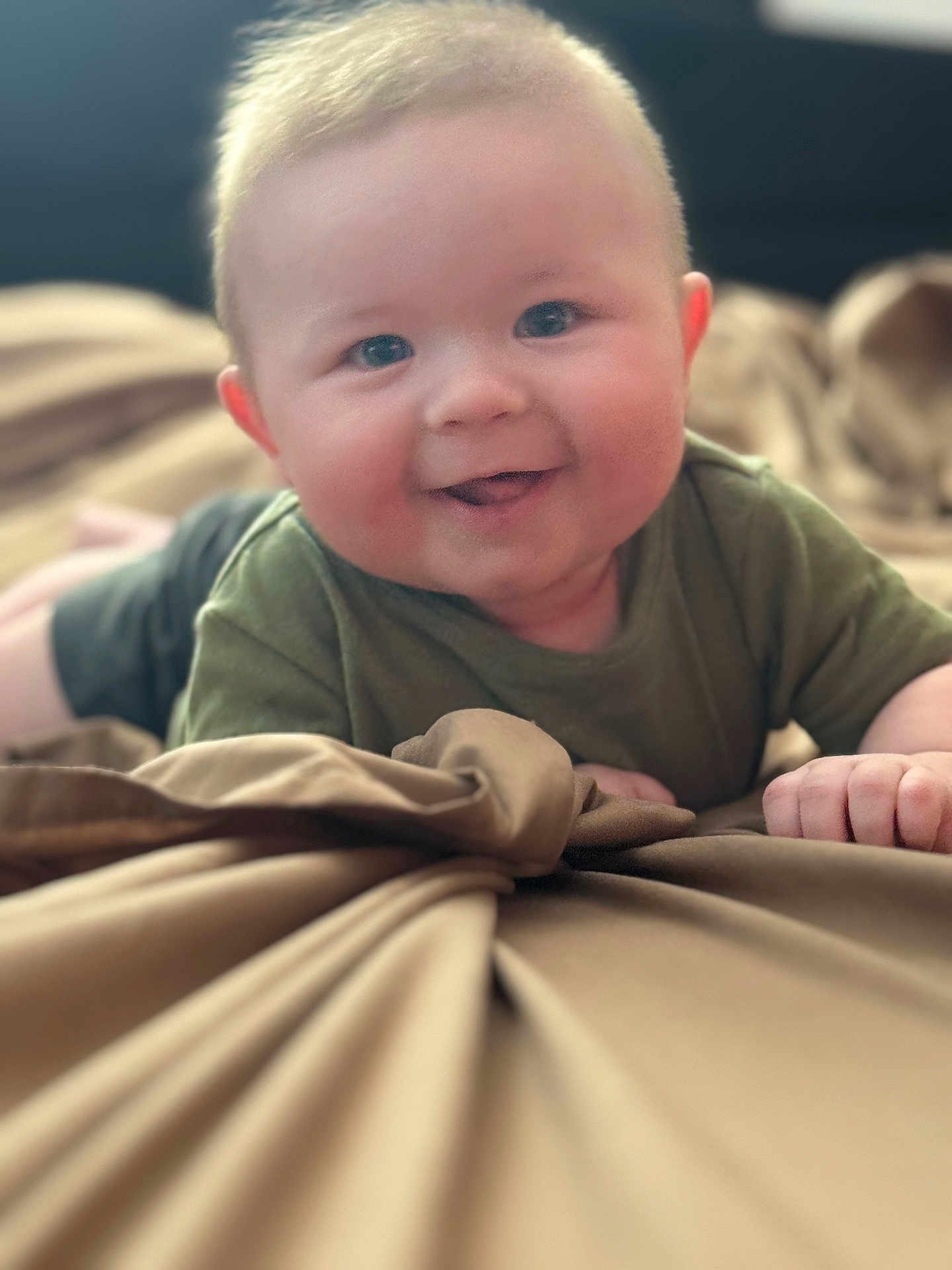 Rayden is registered to the contest to win money with this photo: baby, blanket, child, close_up, clothing, cute, face, green_shirt, hand, happy, indoors, infant, lying_down, person, portrait, skin, smiling, soft_texture, tongue, young
