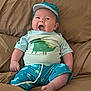 baby, cap, child, clothing, comfortable, couch, cute, dinosaur, funny_face, furniture, happy, indoors, infant, person, portrait, relaxing, shorts, sitting, smile, tshirt