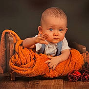 Liam a rejoint le concours — aidez-le/la à gagner de superbes lots ! baby, child, blanket, orange_blanket, wooden_bed, roses, red_roses, floor, wood_floor, portrait, indoor, cute, infant, waving_hand, serious_expression, cozy, wrapped, plush, studio_photo, person