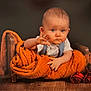 baby, child, blanket, orange_blanket, wooden_bed, roses, red_roses, floor, wood_floor, portrait, indoor, cute, infant, waving_hand, serious_expression, cozy, wrapped, plush, studio_photo, person