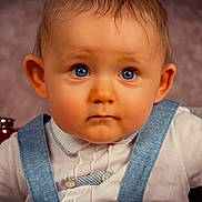 Liam participe au concours pour gagner de l'argent avec cette photo : baby, blue_eyes, child, close_up, clothing, curious, cute, expression, face, hair, indoors, infant, overalls, person, portrait, skin, small_hand, studio, white_shirt, young_child