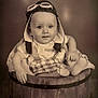Liam participe au concours pour gagner de l'argent avec cette photo : baby, child, infant, aviator_hat, goggles, wooden_barrel, sepia, vintage, portrait, smile, cute, sitting, clothing, feet, hand, face, studio, background, curious, young