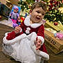 toddler, child, holiday_dress, christmas_tree, christmas_decorations, toys, floor, smiling, red_dress, white_fur_trim, festive, indoors, happy, young_child, christmas_bow, gift_box, holiday_season, cute, celebration, portrait