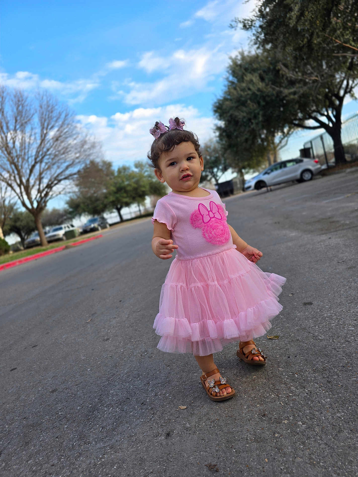Amada is registered to the contest to win money with this photo: toddler, child, pink_dress, butterfly_clips, sandals, outdoor, pavement, trees, car, sky, curious_expression, person, summer, fashion, cute, walking, nature, daylight, young_child, portrait