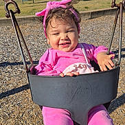 Amada is registered to the contest to win money with this photo: baby, child, clothing, cute, face, hair, happy, headband, metal_chain, outdoor, park, pink_clothing, playground, portrait, smile, sunny, swing, swing_seat, toddler, wood_chips