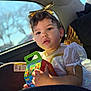 Amada is registered to the contest to win money with this photo: child, toddler, car_interior, car_seat, costume, angel_wings, gold_headband, gold_bow, sparkly_dress, holding_toy, toy_box, portrait, natural_light, blurred_background, curly_hair, earring, expressive_eyes, car_window, sunlight, candid_photo