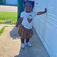 Kaylani is registered to the contest to win money with this photo: toddler, child, outdoor, smile, happy, girl, white_shirt, leopard_skirt, sandals, braided_hair, beads, garage_door, concrete, sunlight, shadow, green_grass, trash_bin, residential, daytime, casual_clothing