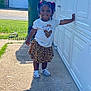 toddler, child, outdoor, smile, happy, girl, white_shirt, leopard_skirt, sandals, braided_hair, beads, garage_door, concrete, sunlight, shadow, green_grass, trash_bin, residential, daytime, casual_clothing