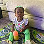 toddler, child, indoor, sippy_cup, play_mat, carpet, couch, white_shirt, green_pants, pouting, funny_face, sitting, toy, floor, home, cute, expression, footwear, hair_bow, person