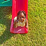 beaded_hair, child, curious, cute, daylight, fun, grass, green_grass, outdoor, park, play, playground, shoes, slide, summer, sunlight, toddler, toy, yellow_dress, young_child