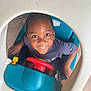 child, smiling, toy_car, steering_wheel, blue, red, white, shorts, tshirt, indoor, play, happy, face, person, looking_up, plastic, floor, cute, boy, seat