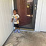child, boy, smiling, standing, bubble_wand, socks, porch, door, glass_door, reflection, concrete, outdoor, daylight, casual_clothing, shorts, tshirt, home, happy, playful, curly_hair