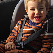 Linda Lecointe a rejoint le concours — aidez-le/la à gagner de superbes lots ! brown_hair, buckle, button, car_interior, car_seat, cheek, child, close_up, clothing, hand, happy, kid, portrait, seat_belt, shadow, smile, striped_sweater, sunlight, teeth, toddler