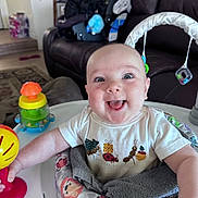 Gunner is registered to the contest to win money with this photo: baby, smiling, toy, baby_seat, indoor, living_room, couch, child, happy, person, clothing, toddler, furniture, play, infant, colorful, face, expression, home, seat