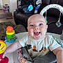 baby, smiling, toy, baby_seat, indoor, living_room, couch, child, happy, person, clothing, toddler, furniture, play, infant, colorful, face, expression, home, seat