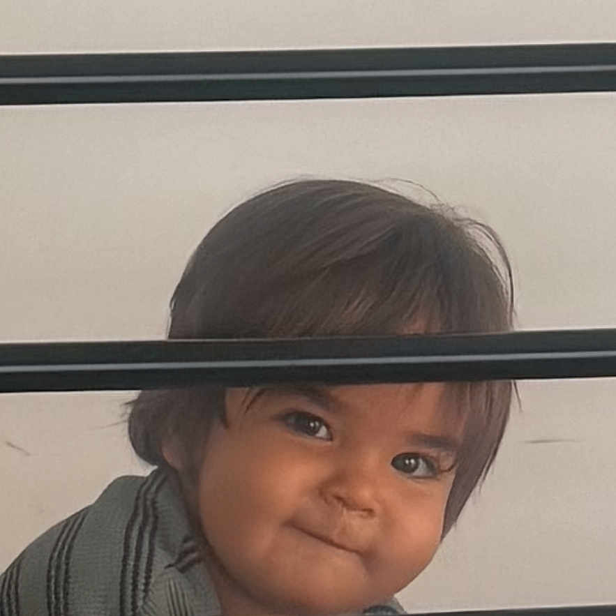 Caeser joined the competition — help win amazing prizes! toddler, child, face, smile, striped_shirt, bars, peeking, curly_hair, indoor, portrait, cute, playful, mischievous, young_child, person, head, expression, clothing, horizontal_lines, background