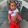 baby, child, girl, sitting, chair, plastic_chair, clothing, onesie, socks, red_socks, skirt, hair_bows, face, eyes, hands, outdoor, wall, expression, nike_logo, cute