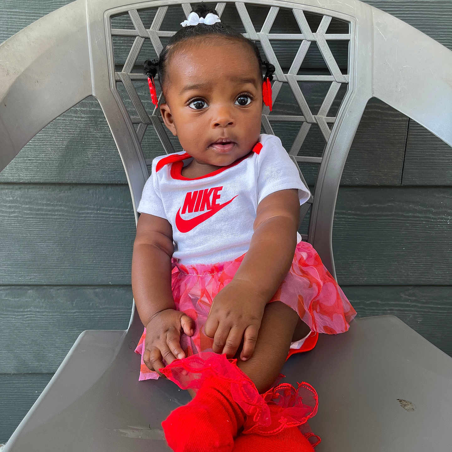 Séyori is registered to the contest to win money with this photo: baby, chair, child, clothing, cute, expression, eyes, face, girl, hair_bows, hands, nike_logo, onesie, outdoor, plastic_chair, red_socks, sitting, skirt, socks, wall