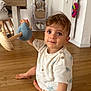 child, toddler, toy, wooden_floor, indoor, high_chair, curious, sitting, clothing, shorts, shirt, wood, furniture, baby, person, floor, home, cute, play, expression