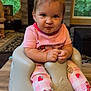 baby, child, infant, pink_clothing, pajamas, strawberry_pattern, baby_seat, table, living_room, television, funny_face, cute, indoors, wooden_table, foot, hands, expression, cozy, carpet, furniture