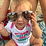 baby, sunglasses, beach, sand, shirt, reflection, blanket, child, person, outdoor, summer, cute, smile, funny_text, casual, feet, skin, hand, sunny, portrait