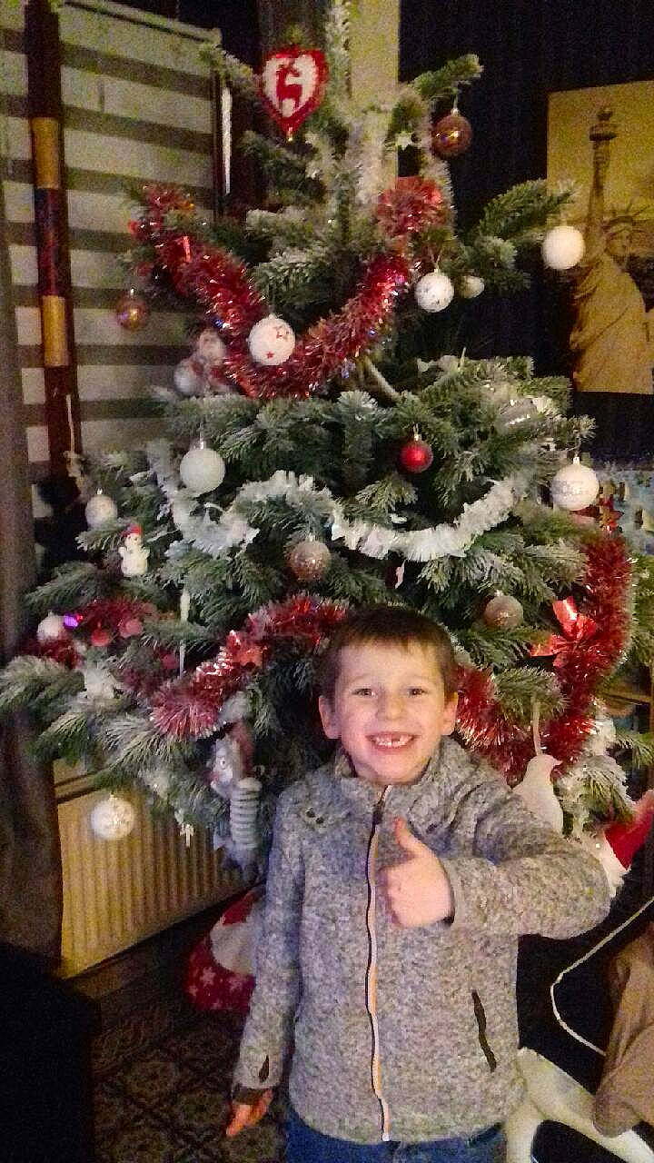 Jules participe au concours pour gagner de l'argent avec cette photo : christmas, christmas_decoration, christmas_ornament, christmas_tree, conifer, event, evergreen, happy, holiday, holiday_ornament, human_body, jacket, joy, ornament, person, plant, red, smile, standing, toddler