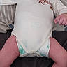 baby, infant, onesie, diaper, bed, pillow, lying_down, face, skin, person, child, newborn, expression, looking, hands, legs, casual, indoor, cute, resting