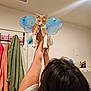 cat, person, indoor, fairy_wings, orange_cat, white_cat, towels, bathroom, holding, playful, pet, animal, feline, decor, wall, vent, hand, ring, hair, light