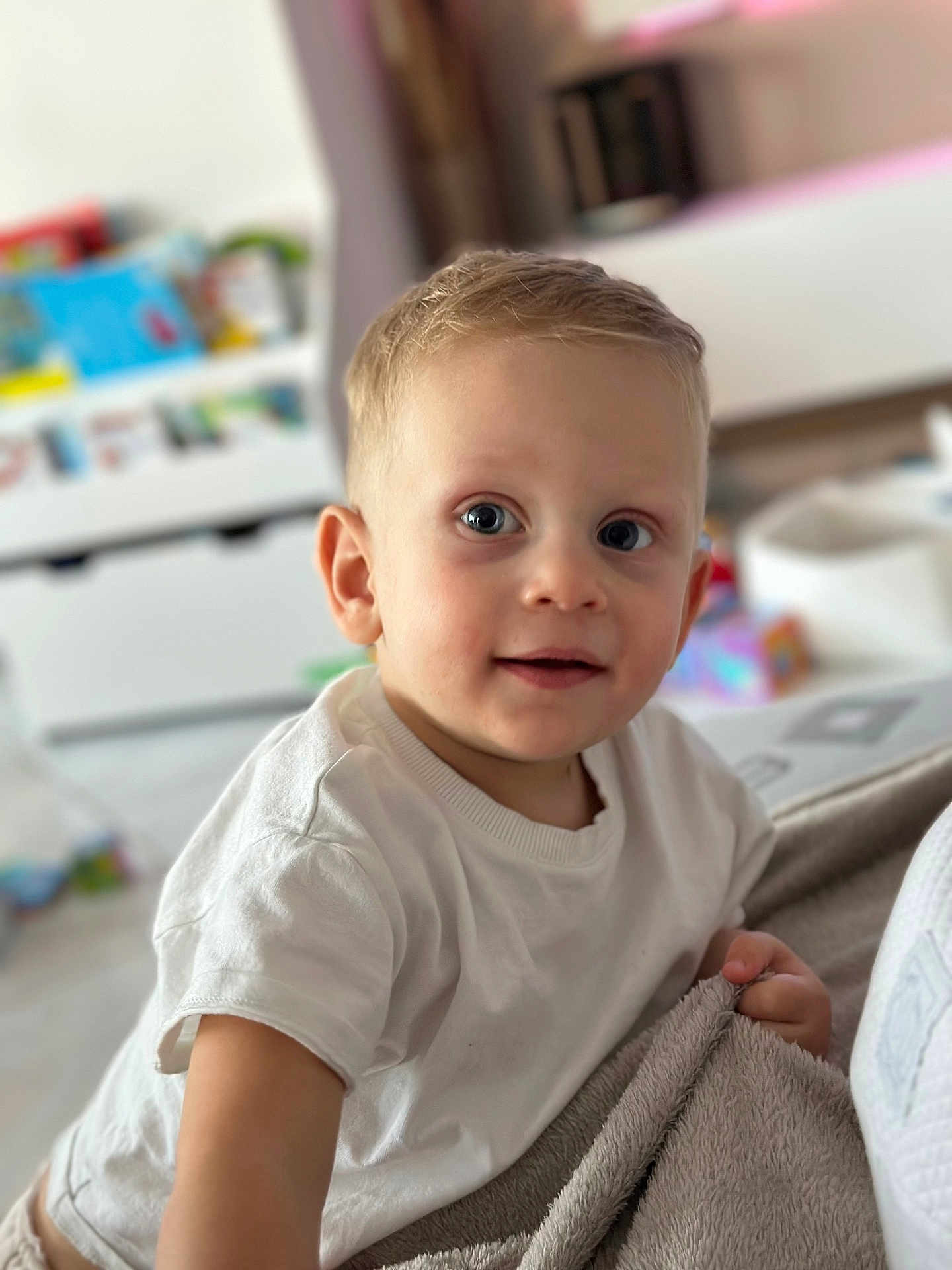 Aaron a rejoint le concours — aidez-le/la à gagner de superbes lots ! toddler, child, white_shirt, blanket, indoor, playroom, curious, face, blue_eyes, short_hair, person, soft_light, portrait, smiling, skin, hand, couch, toy, furniture, baby