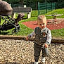 toddler, child, playground, wood_chips, stroller, bench, grass, fence, spring, sunlight, jacket, pants, sneakers, outdoor, walking, park, daytime, person, cute, young